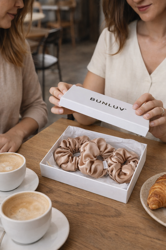 Two women at a table with a box of 'BUNLUV' scrunchies and coffee.