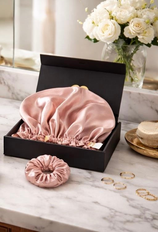 pink and rose gold bunluv gift box set including bonnet and silk scrunchie in a box on a marble countertop with bathroom items in the background.