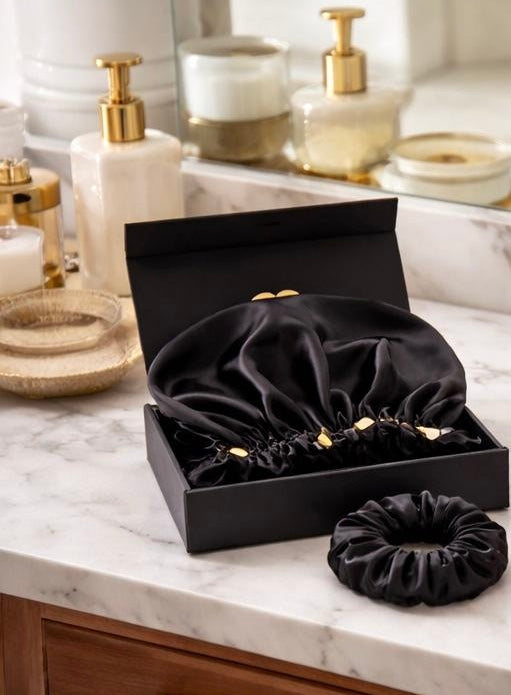 Black bunluv gift box set including bonnet and silk scrunchie in a box on a marble countertop with bathroom items in the background.