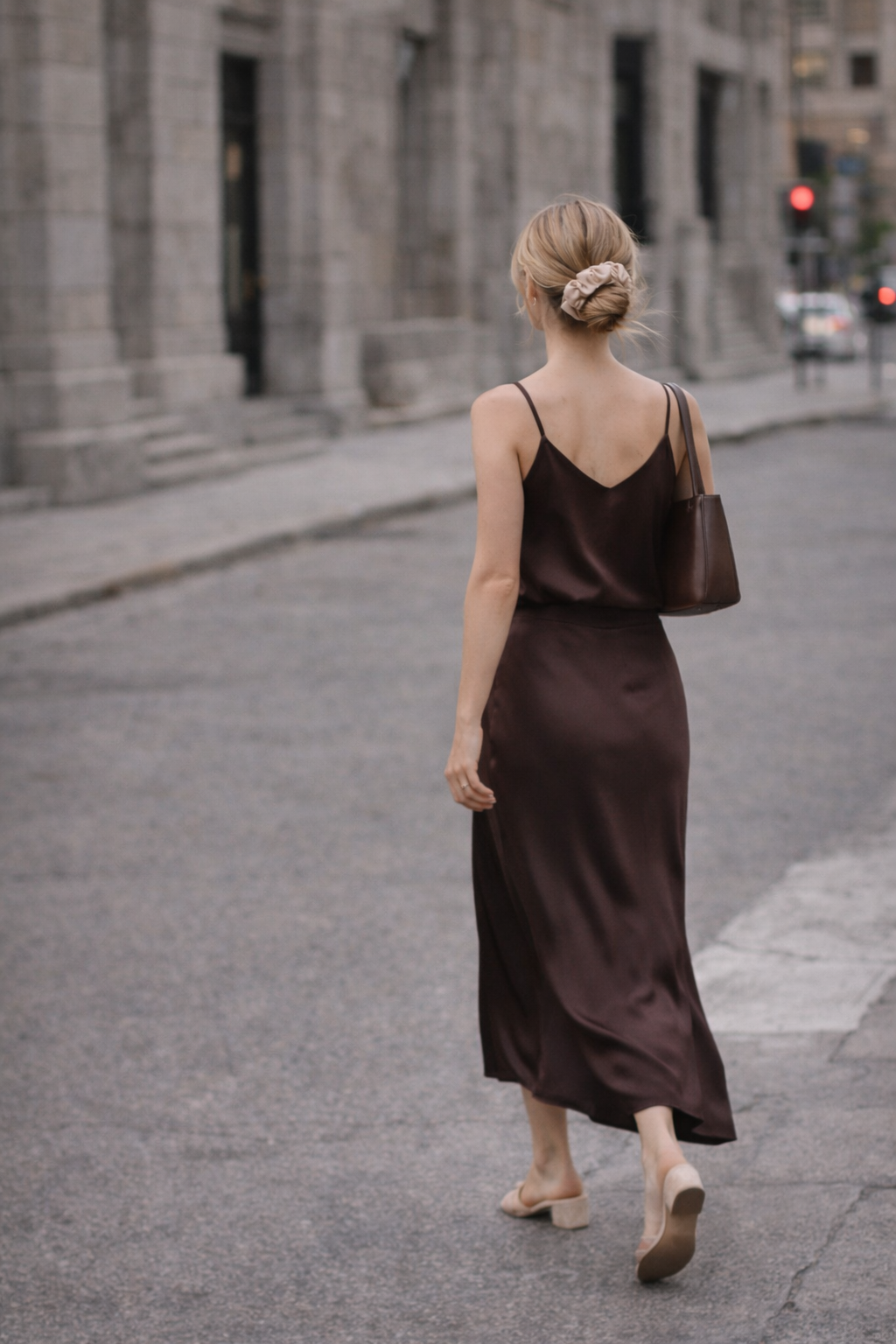 Woman wearing a BUNLUV spiral scrunchie in a low ponytail, walking away in natural light