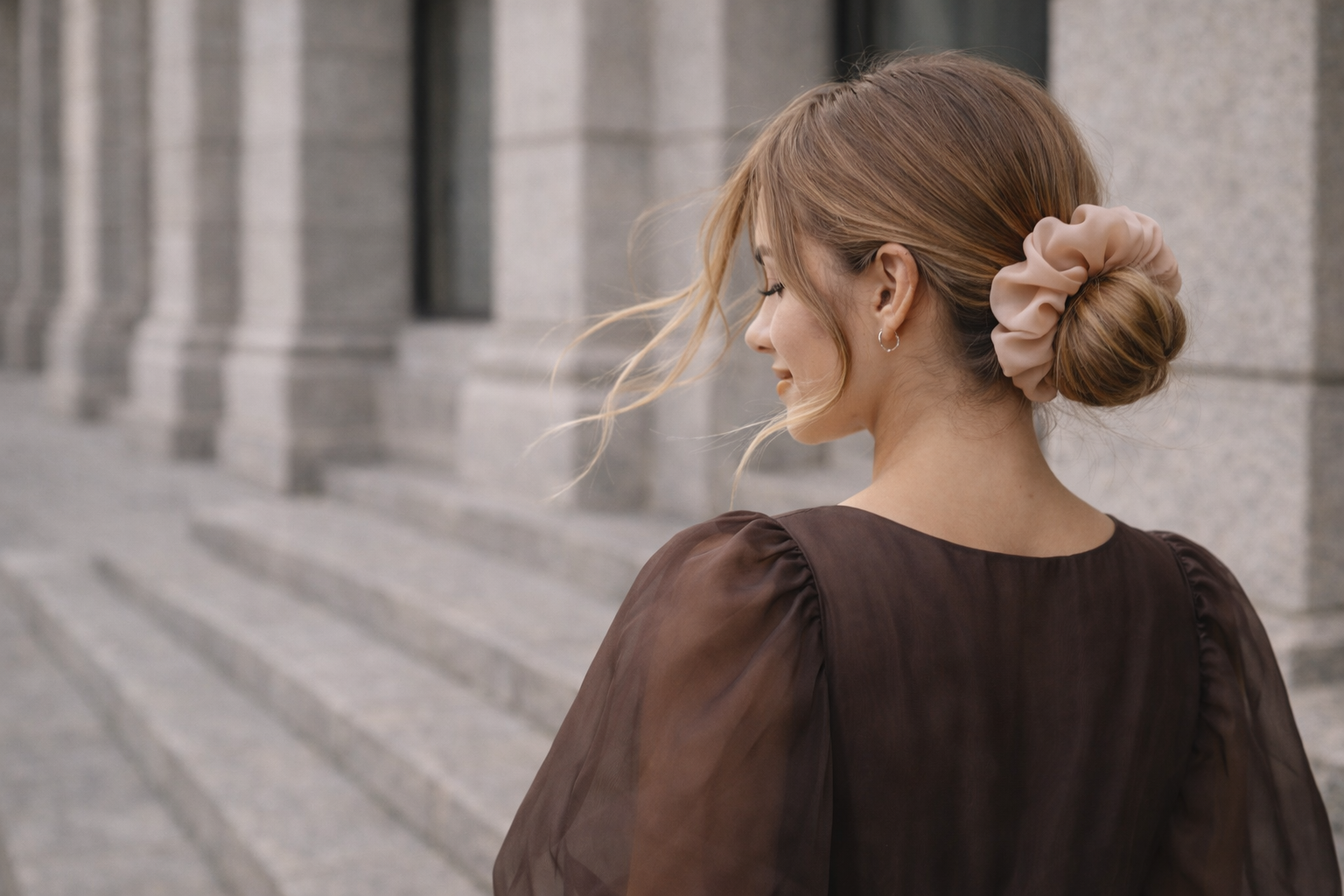 Woman with a bun wearing a brown top in front of a building wearing bunluv silk scrunchie for everyday wear