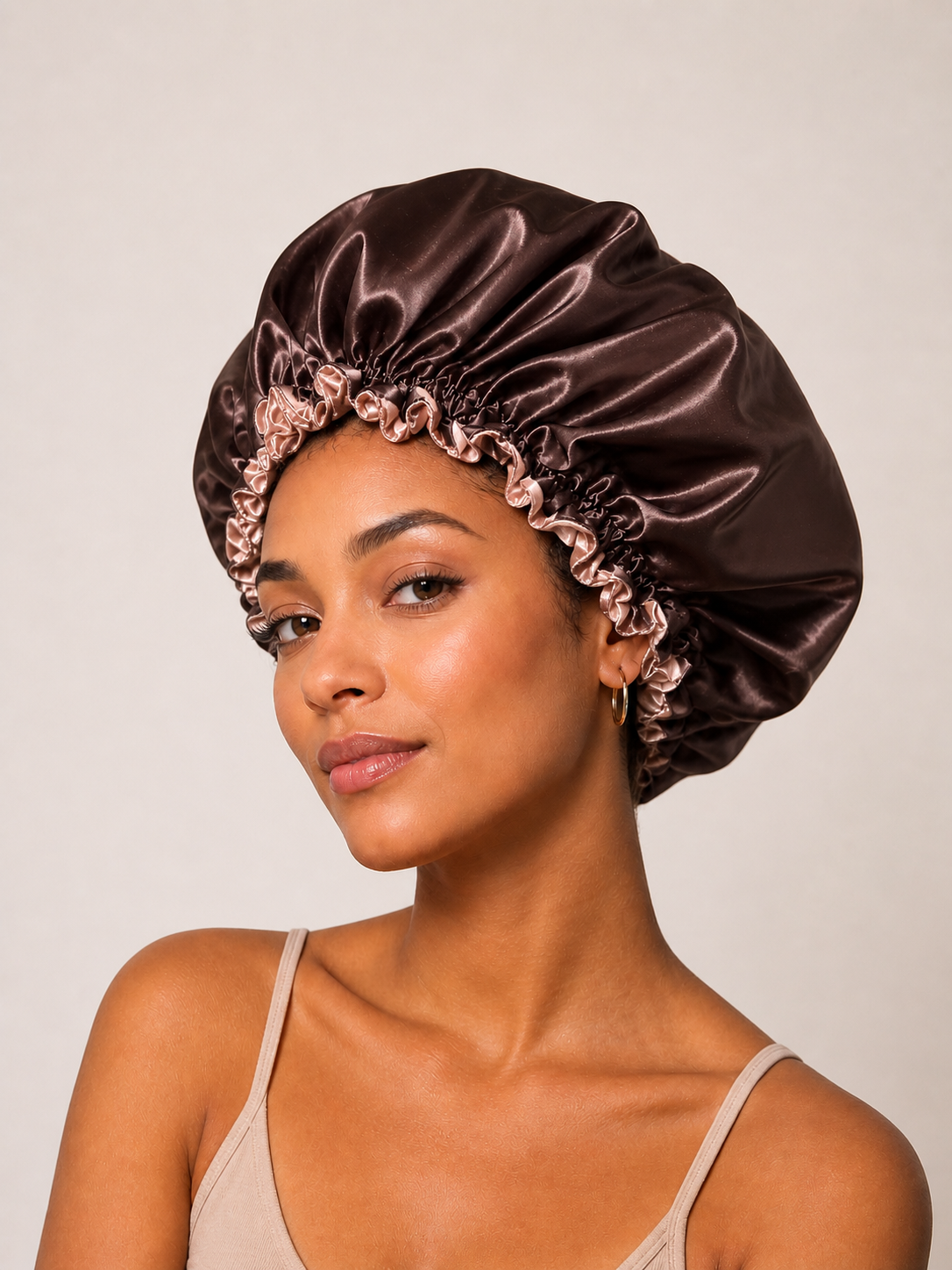 Woman wearing a dark chocolate and rose gold satin bunluv bonnet against a plain background