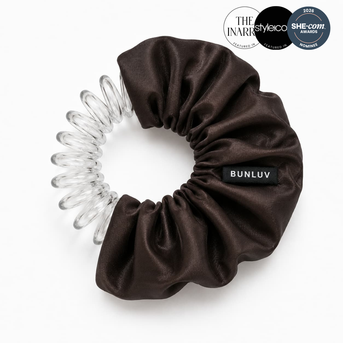 A dark brown silk smartcore spiral hair scrunchie with a clear coiled spring attachment on the side, featuring a black label that reads 'BUNLUV'. One award badge and two feature badges for the product are displayed in the top right corner from style icons, the inarra and SHE-com