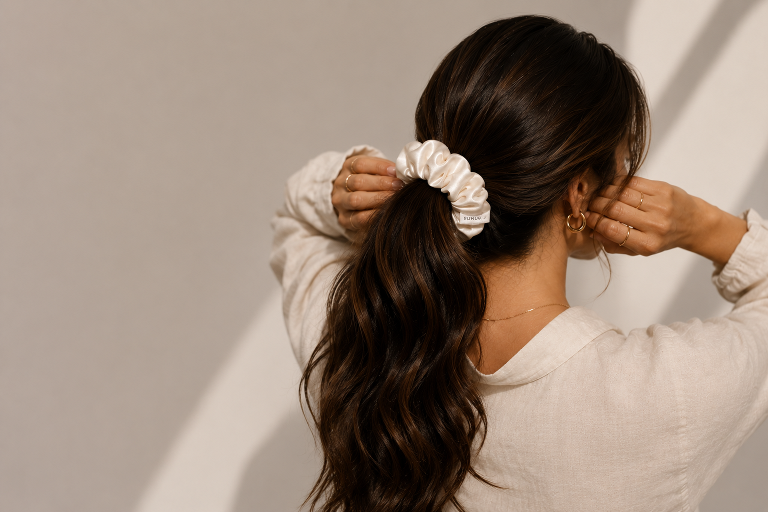 Woman with a ponytail wearing a BUNLUV white smartcore spiral scrunchie against a neutral background
