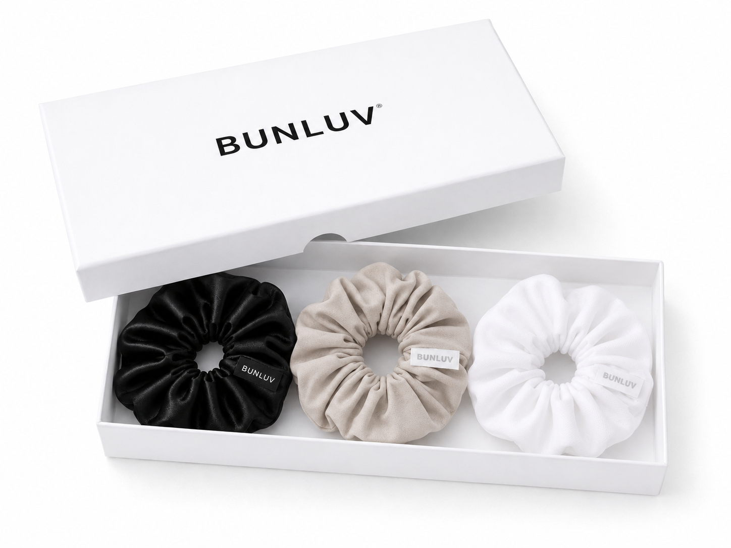 Three BUNLUV scrunchies in black, nude and white are displayed in a white gift box with the lid propped open, which features the BUNLUV brand name.