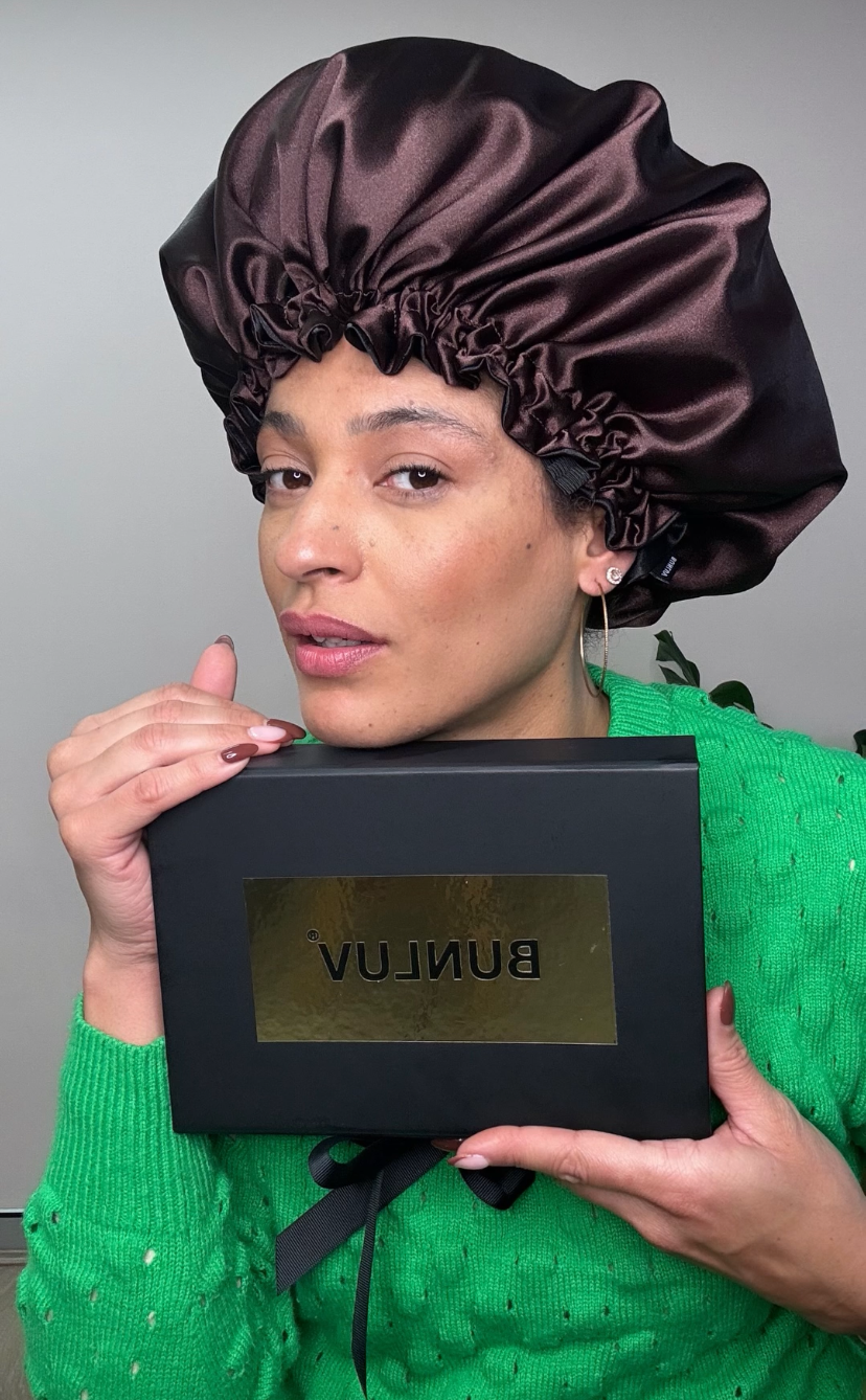 Unique hair me owner holding a black box with BUNLUV branding, wearing a brown satin bonnet.