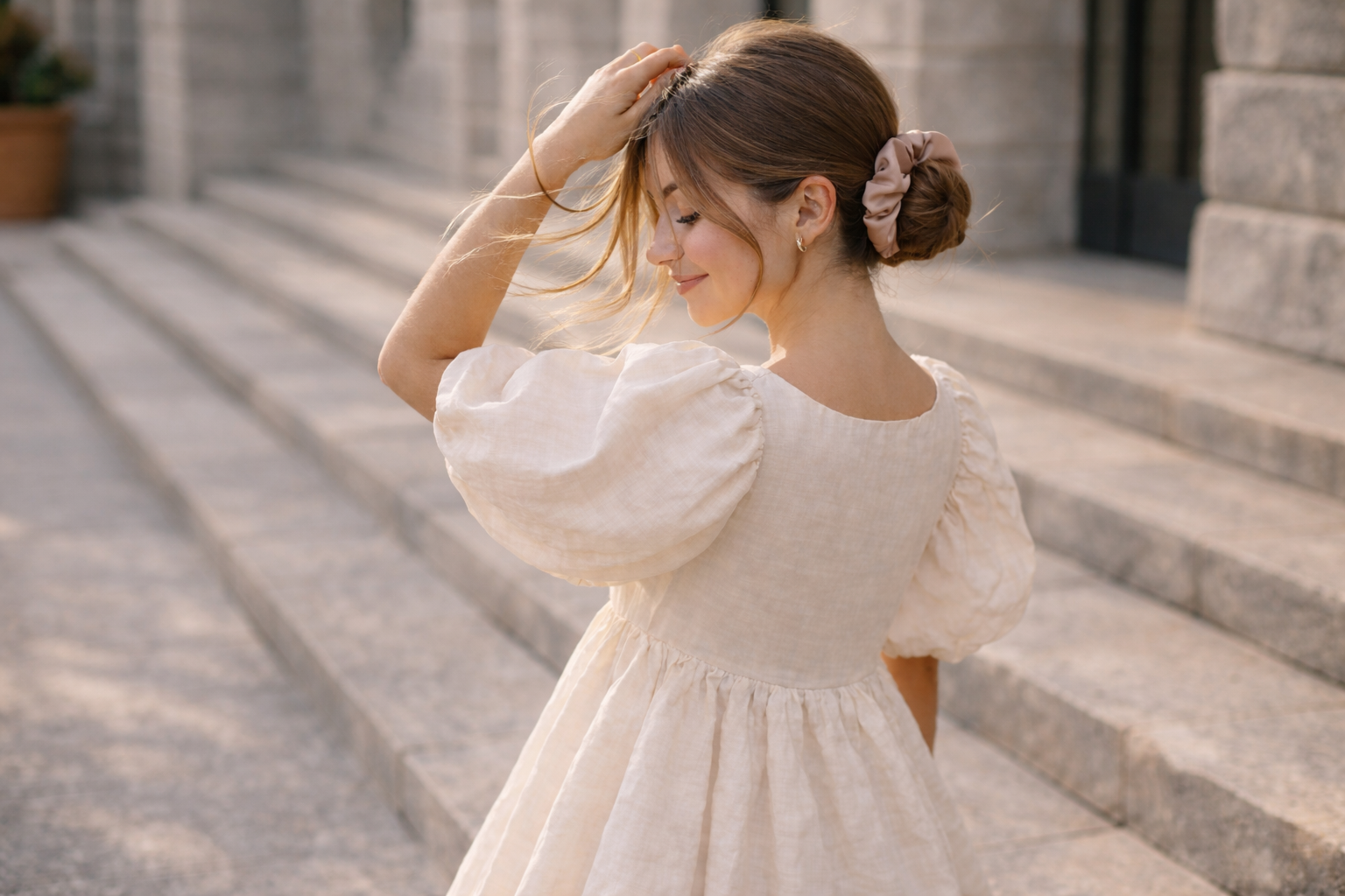 Woman in a white dress wearing bunluv scrunchie standing on stone steps outdoors